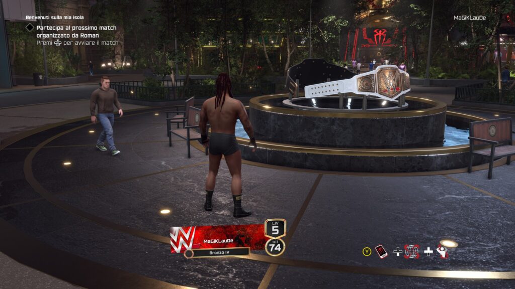 Uno screenshot della modalità The Island di WWE 2K25 con un wrestler di spalle al centro di una piazza popolata da personaggi in abiti civili. 